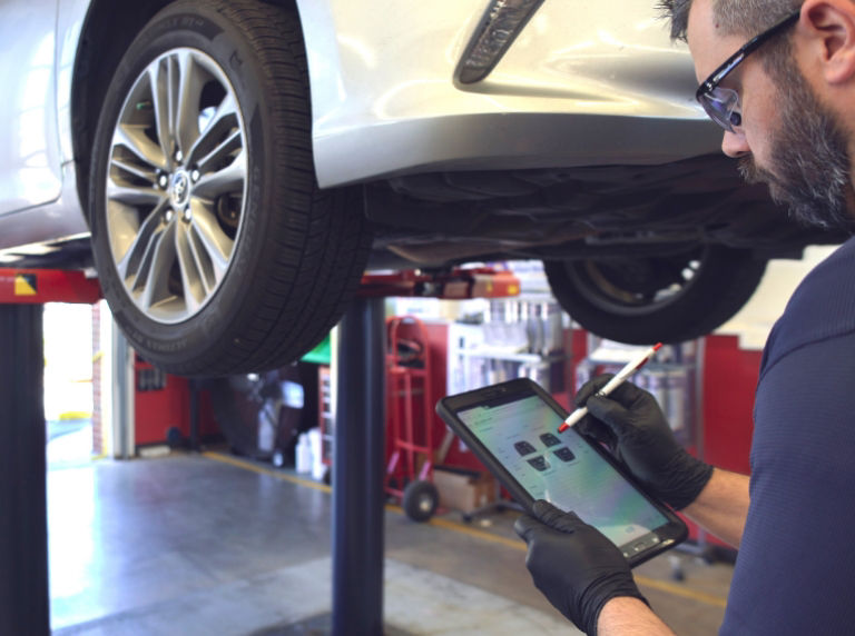 Mechanic inspecting car on shop lift.