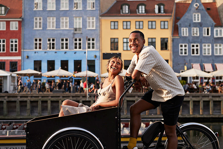 Happy young man with girlfriend in cargo bike at famous pier in Europe.