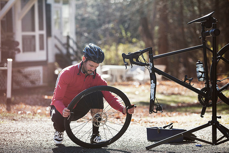 A cyclist wearing a helmet uses a smartphone next to a bicycle in an urban setting. 