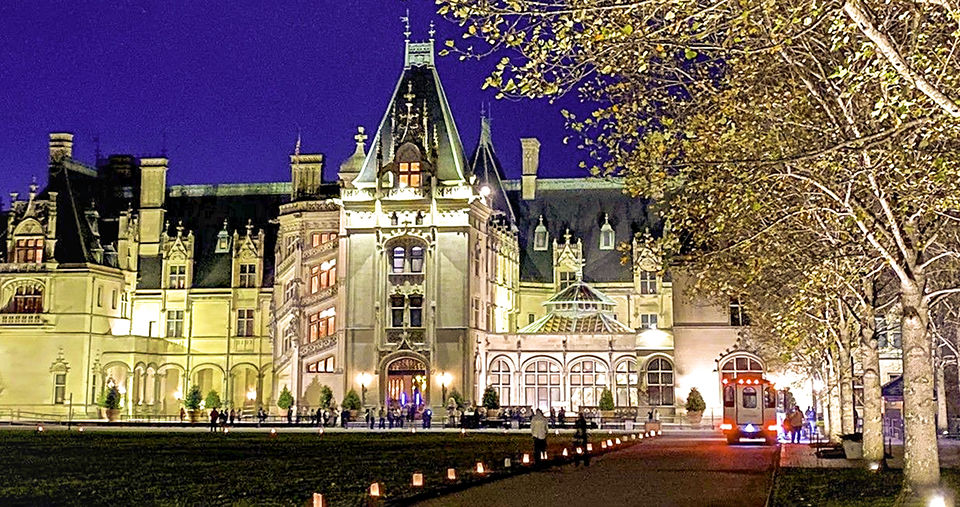 A vertical shot of a Biltmore and garden at night with lights during Christmas