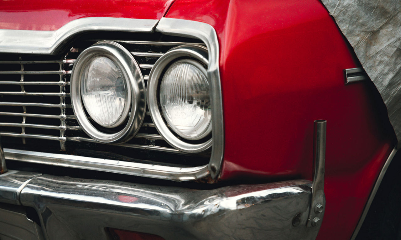 Classic American retro car under car case on the street. Bumper and headlight of red vintage car