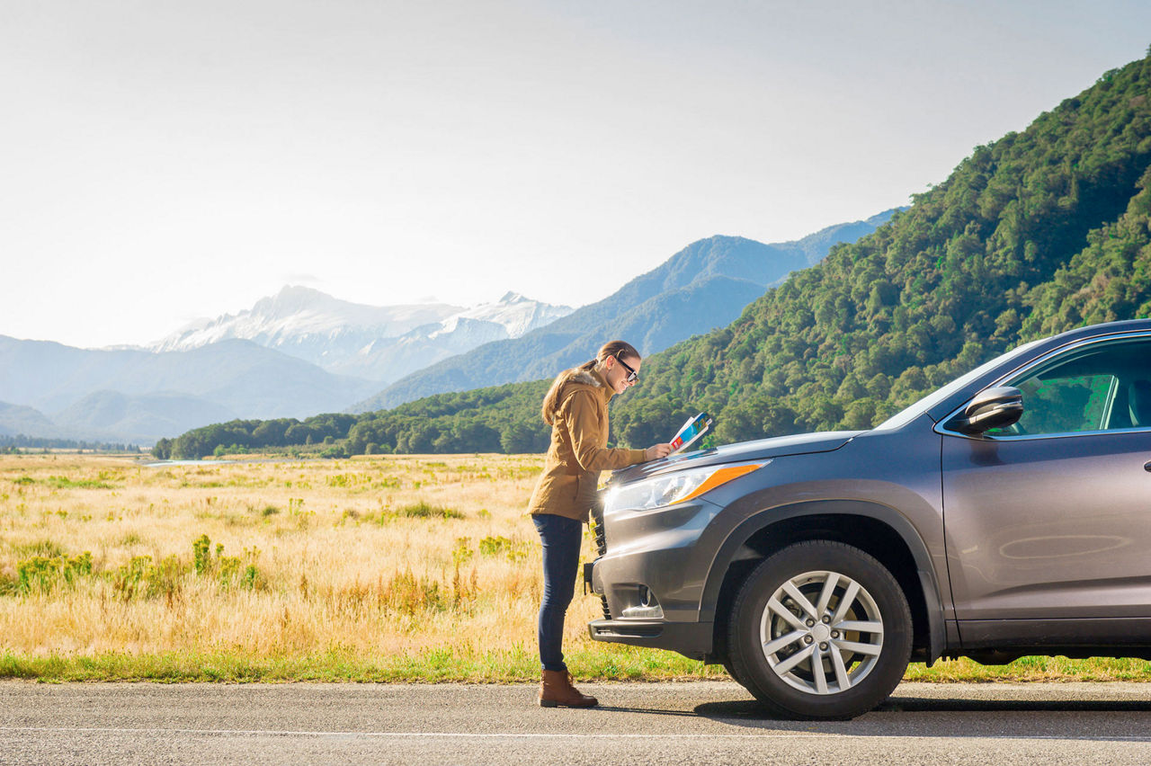 Caucasian woman looking at the map, next to her car.