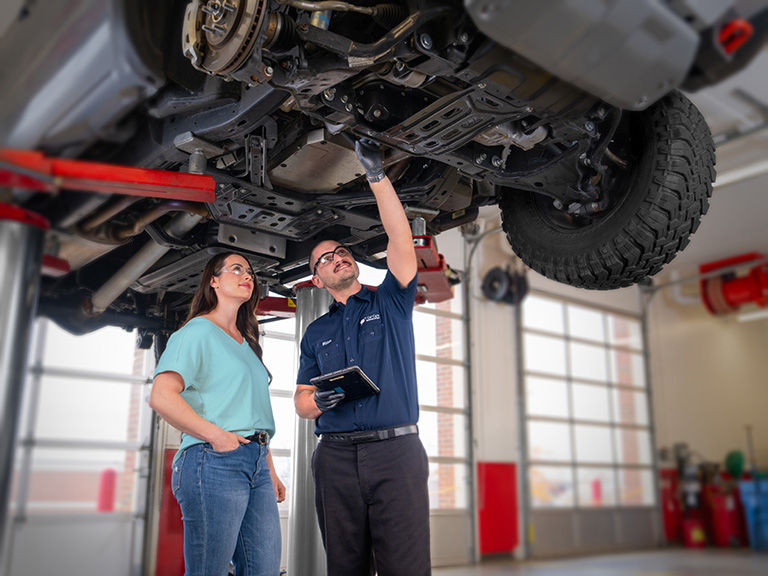 Mechanic with a customer underneath her car up on a hoist at a repair facility.