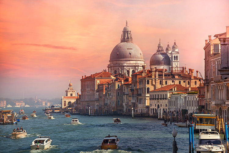 Small boats sail through the water in venice italy during a beautiful pink sunset.