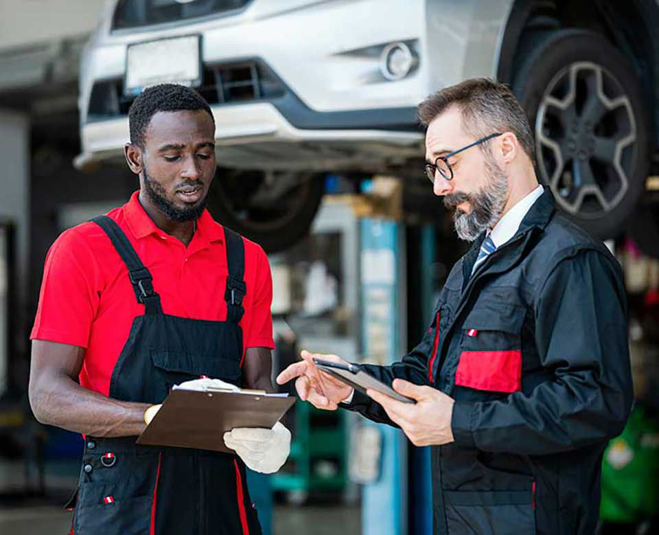 Insurance claims agent is reviewing the cars damage with a worker at the mechanics shop.