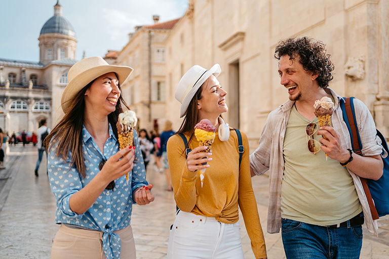 Three Young Friends Eating Ice Cream While Walking On The Street Dubrovnik.