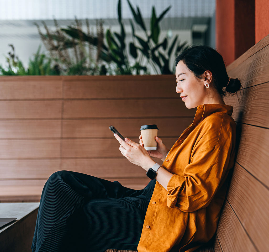 Young Asian woman sitting in a sidewalk cafe with a cup of coffee and using her smartphone to pay for her membership. 
