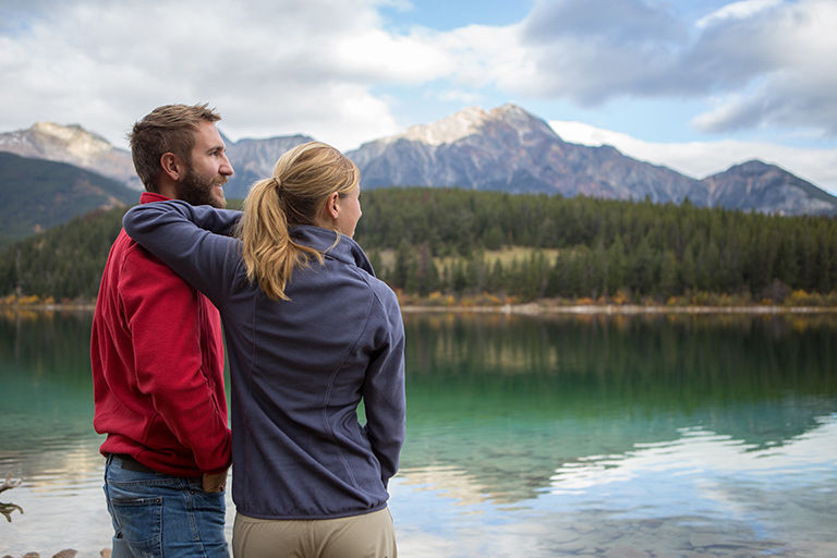 Young cheerful couple hiking by the lake in Autumn, they are having a break looking at the beautiful landscape.