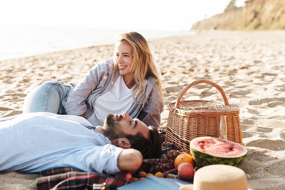 Cheerful young couple in love having picnic at the beach, relaxing