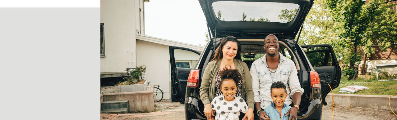 Portrait of smiling multi-ethnic family leaning on car trunk in front yard