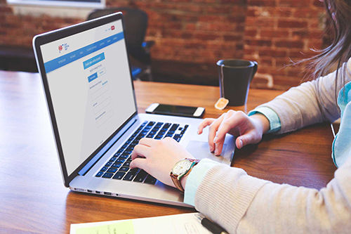 Women sits at a table with her laptop creating her AAA online account.
