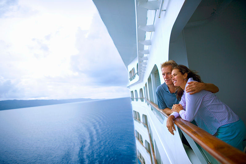 A couple embracing on along the deck railing of a cruise ship looking at the sea.