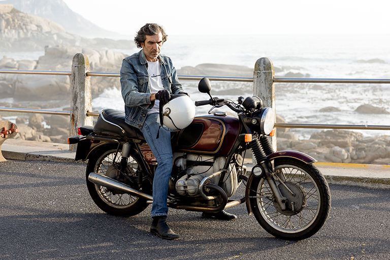 Man adjusting his helmet next to his vintage motorcycle.