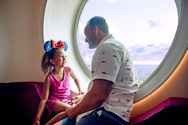 Father and daughter sitting near port hole window of cruise ship