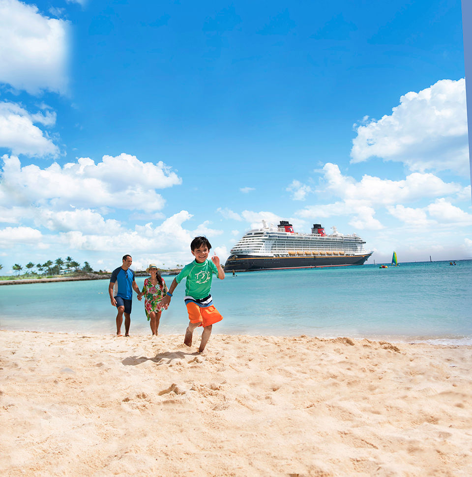 Family running on beach with a Disney Cruise ship docked in the background.