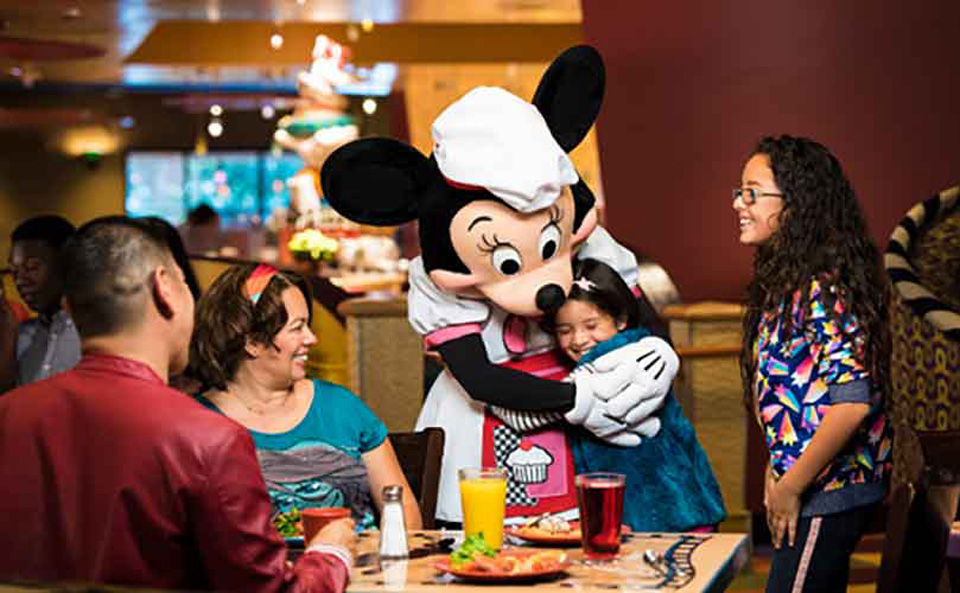 Minnie mouse hugs little girl at a dining with the characters. 