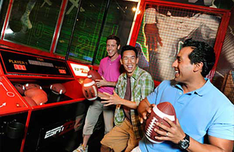 Three men play a football game in the espn zone at disneyland.