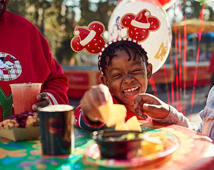 Little boy with christmas mickey mouse ears eats chips and salsa smiling and laughing.