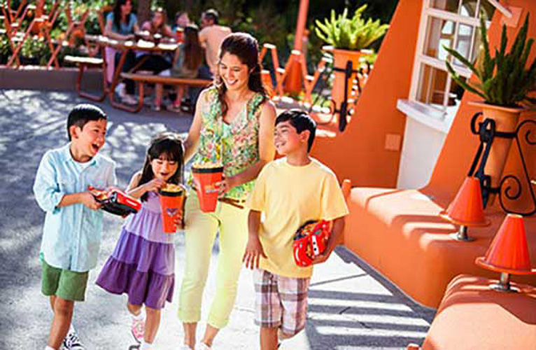 Mother walks with her three kids as the boys hold onto lighting macqueen toys and the daughter eats popcorn.