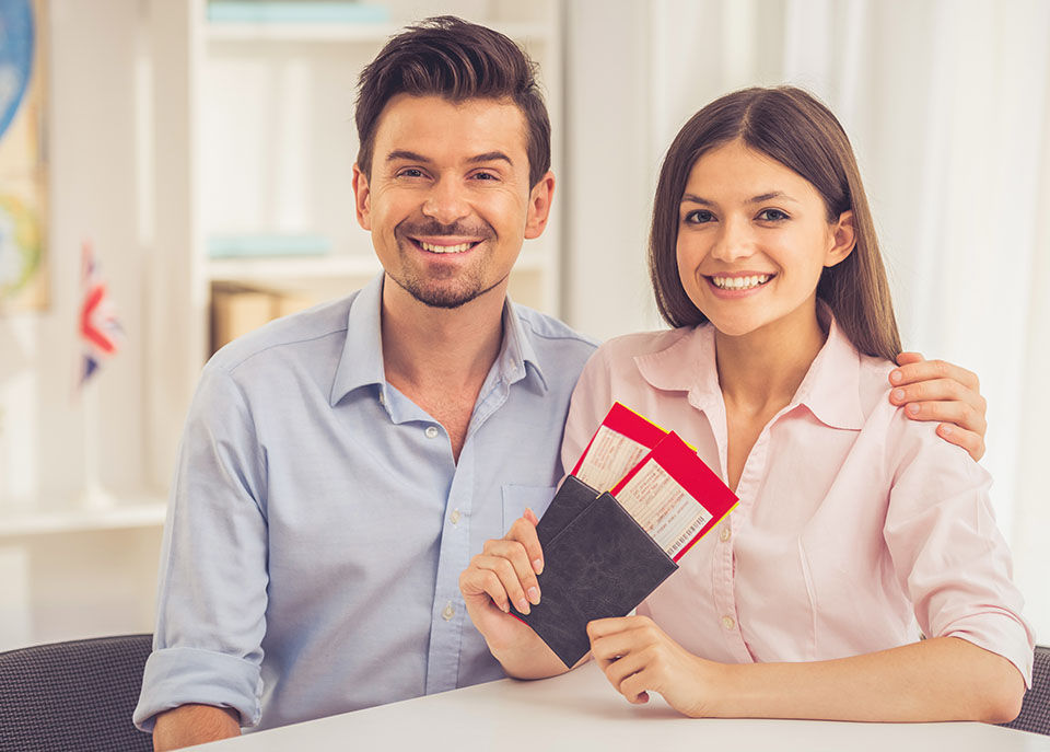 Beautiful happy young couple is holding tickets and documents, looking at camera and smiling while sitting in travel agency