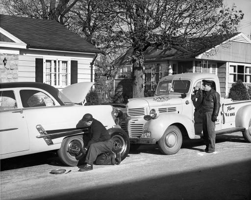 Historical photo of a repair technician servicing a vehicle in a neighborhood