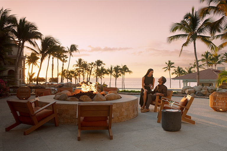 A couple at sunset next to the fire pit at Dreams Los Cabos Resort & Spa