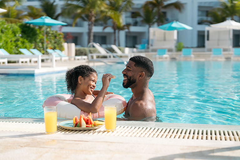 Daughter and father, enjoying snacks and tropical fruit while relaxing in a luxury resort pool.