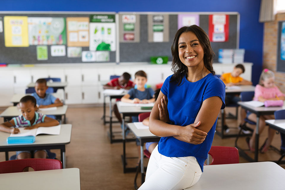 Teacher smiling, in the classroom, with children in the background.