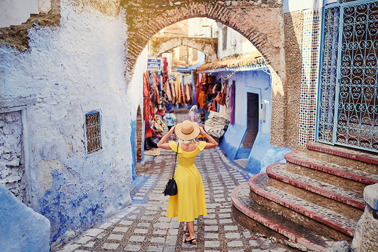 Colorful traveling by Morocco. Young woman in yellow dress walking in  medina of  blue city Chefchaouen.