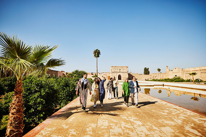 A group of tourists in a desert location looking at some ancient ruins near a lake.