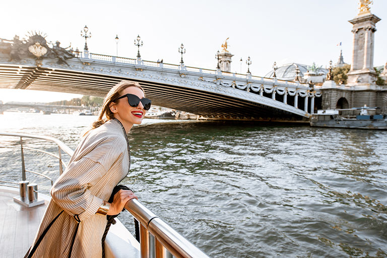 Young woman enjoying beautiful landscape view on the riverside from the tourist ship during the sunset in Paris.