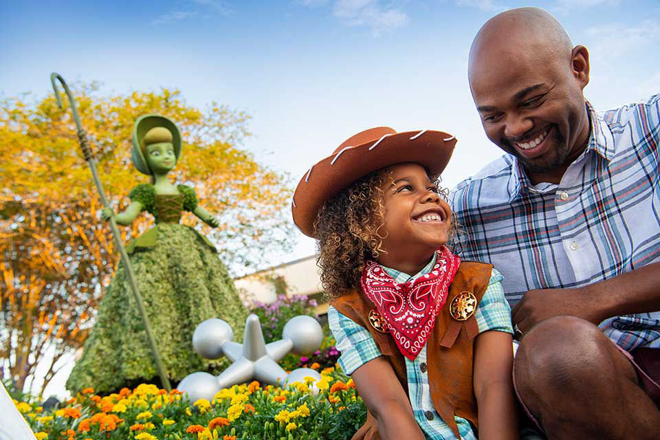 Father and son smiling and sitting on ledge with a flower toy story character behind them.