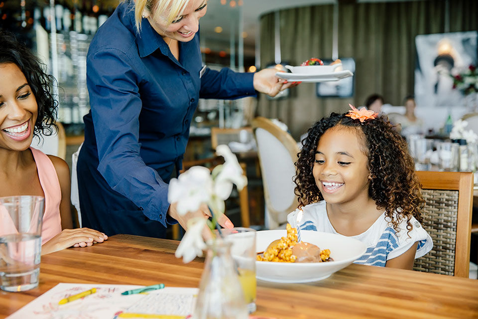Young girl with her mom, smiling, while the waiter serves them their food.
