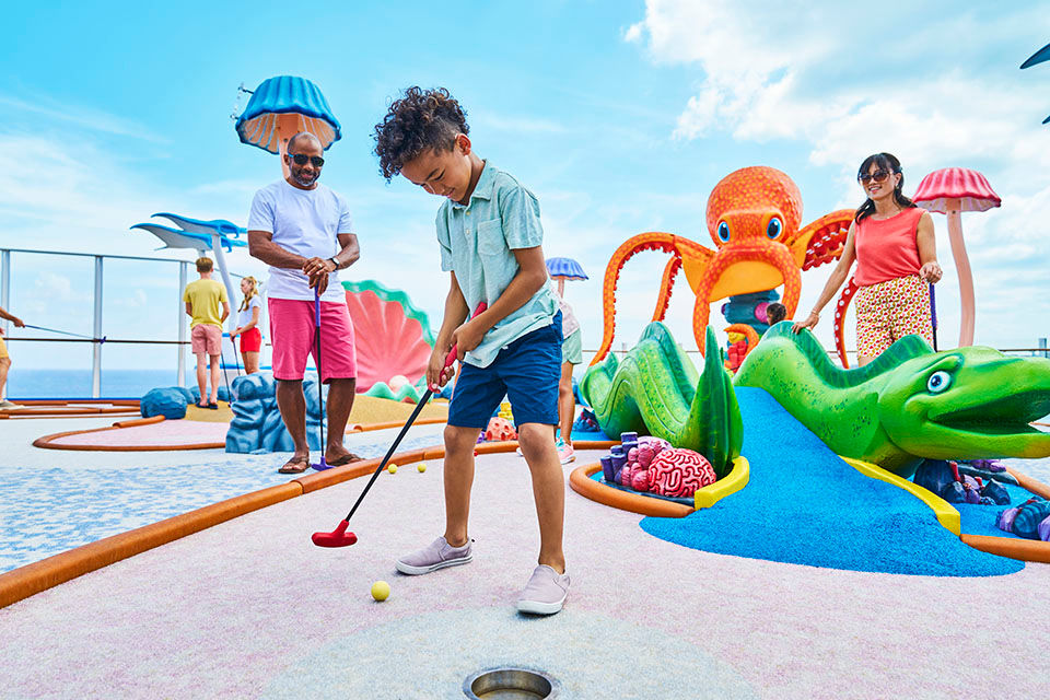 WN, Wonder of the Seas, Brand shoot, young boy, kid, about to make a putt shot in Dunes, mom and dad watching, mini-golf, mini golf, orange octopus and green snake figures in background, family fun,