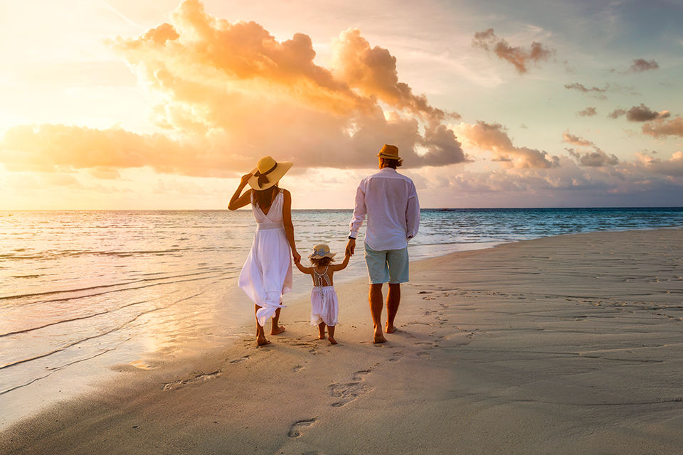 A family walks hand in hand down a tropical paradise beach during sunset.