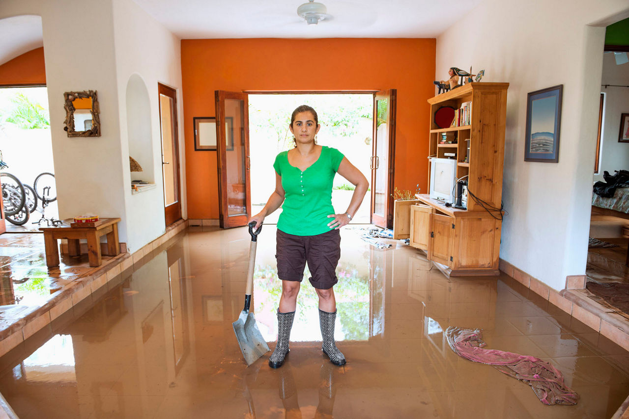 Hispanic woman shoveling water out of flooded house.
