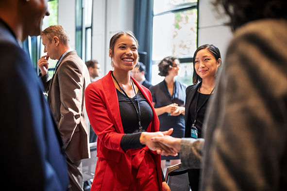 Confident businesswomen handshaking while standing in corridor of an auditorium. Female professionals greeting each other convention center.