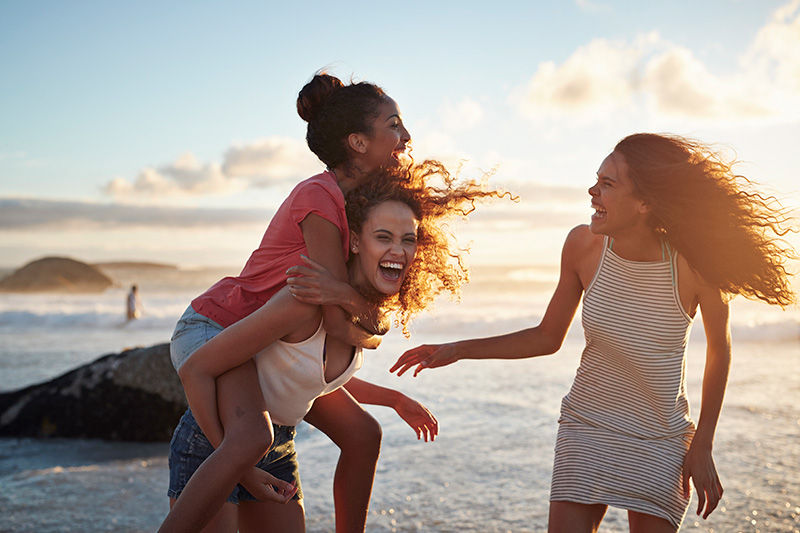 Three young women smiling laughing and playing on a beach.