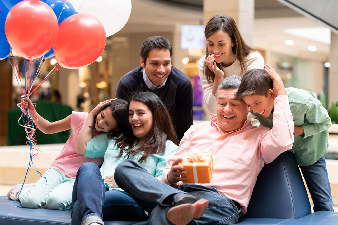 Happy grandfather celebrating Fatherâ  s Day with his family at the mall and holding a gift while smiling â   lifestyle concepts