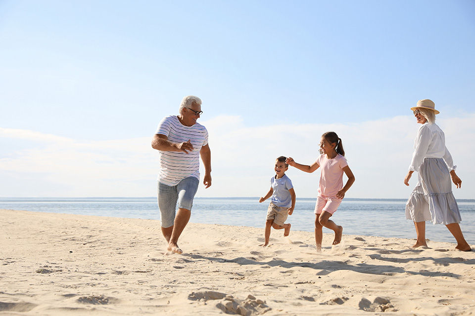 Multi-generation family running and laughing on a sunny beach by the ocean