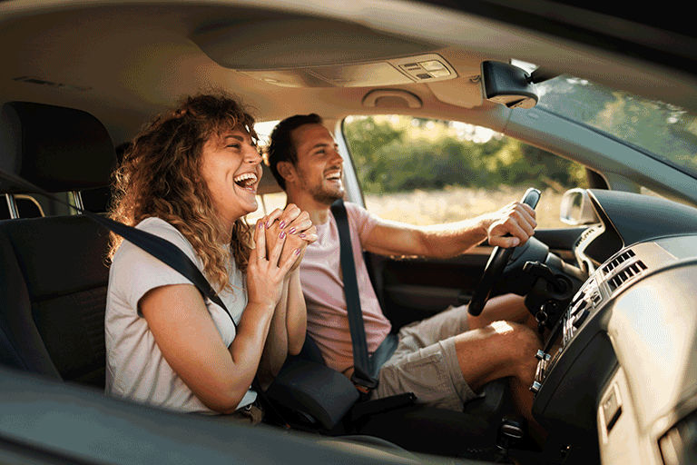 A couple on a road trip laughing while driving.