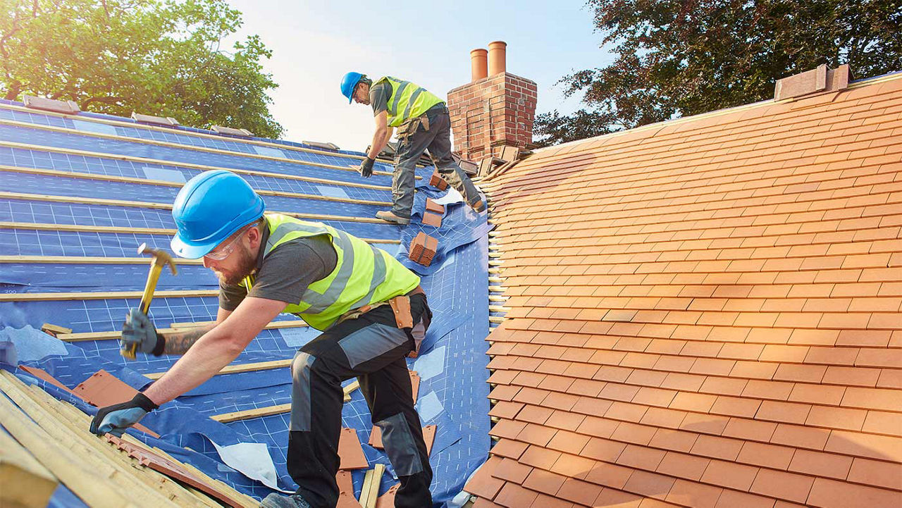 Two men working on a roof applying shingles and other materials to it.