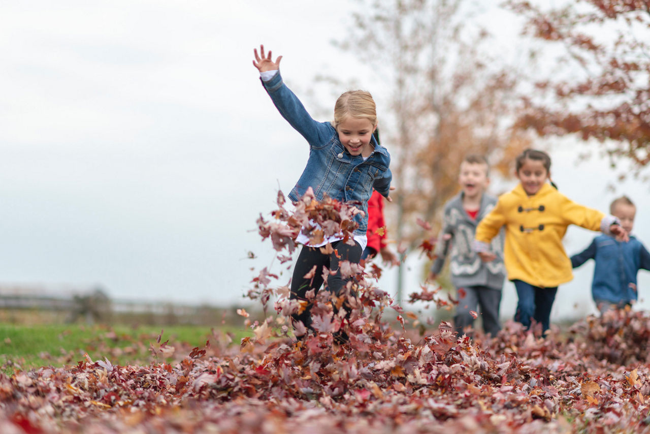 Kids running and jumping in a leaf pile.