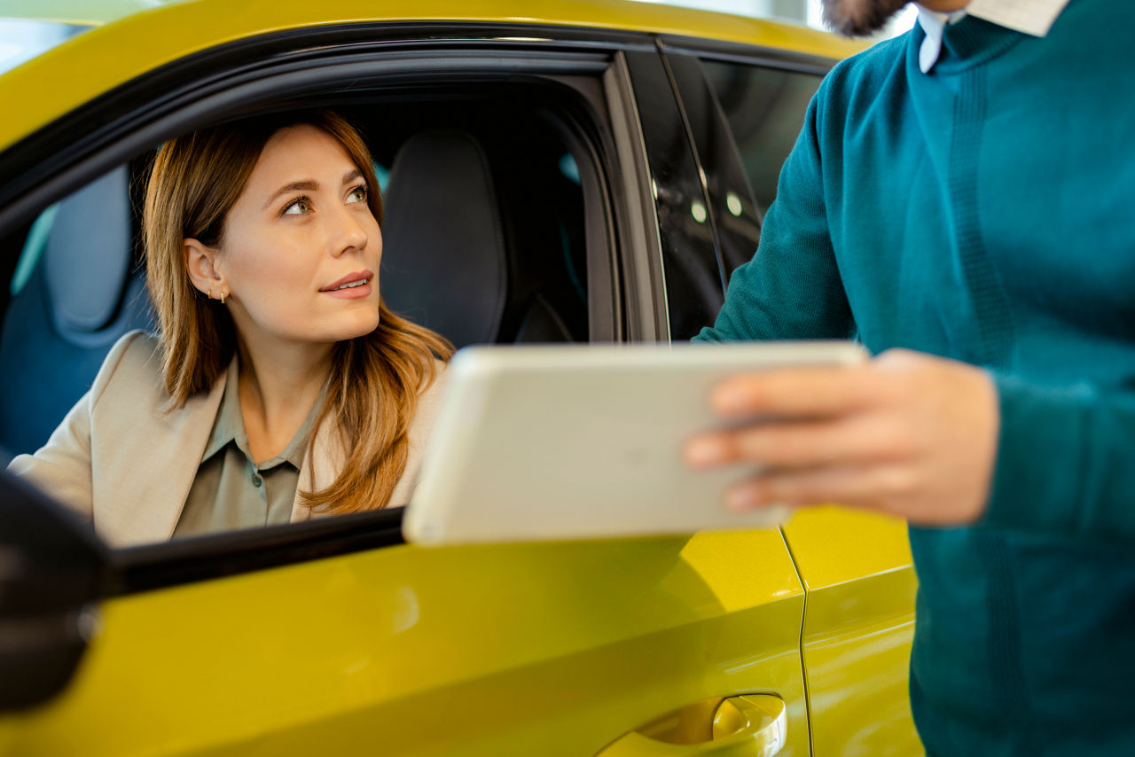 woman looking out her car windown to a man showing her something on tablet