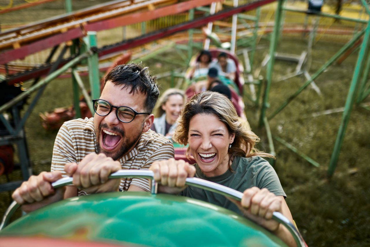 Young carefree couple having fun on rollercoaster ride at amusement park.