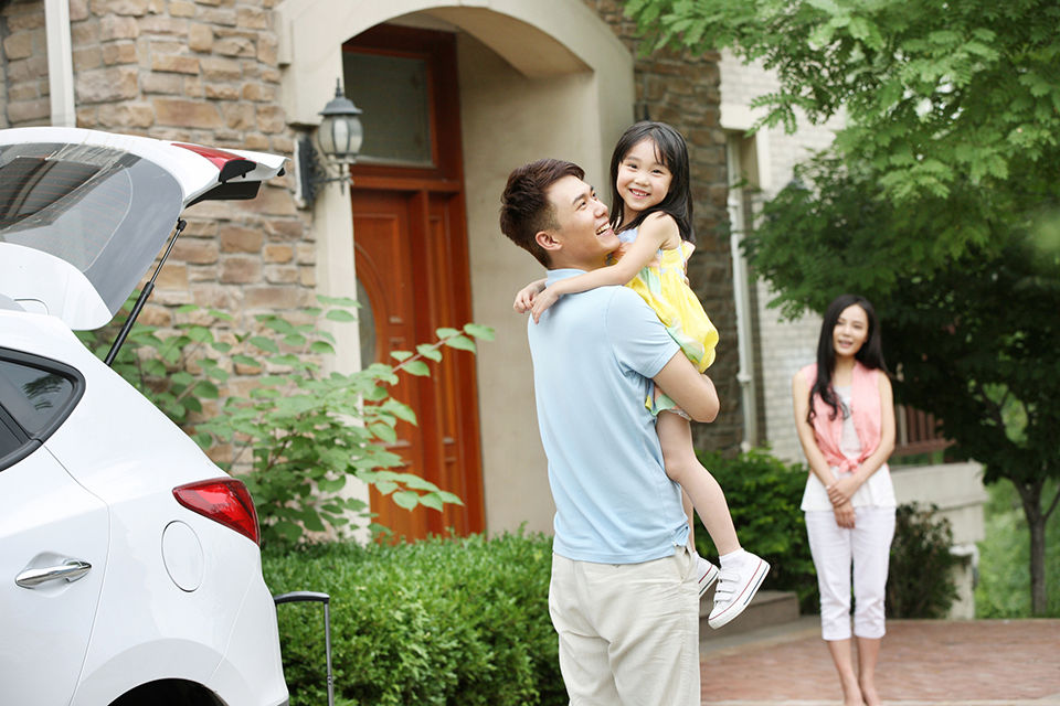Family next to their car, in front of the house. Smiling.