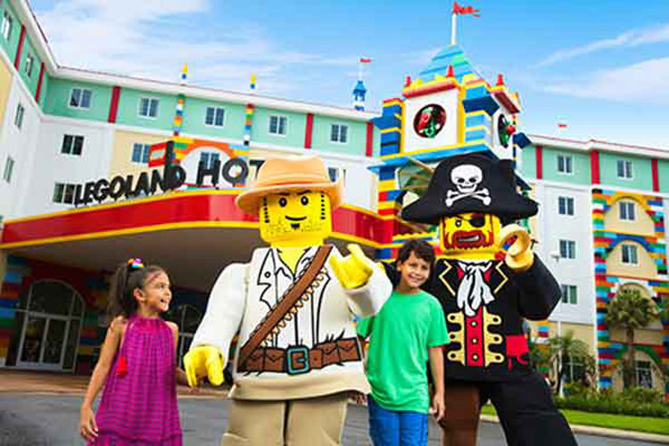 Two kids with legoland characters pose outside the legoland hotel.