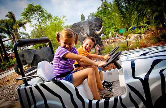 Two kids ride zebra print jeep on the shuttle ride to the legoland park .