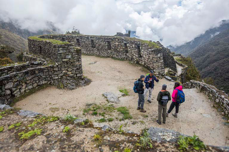 Hikers walking through Machu Picchu stone ruins under misty mountain clouds