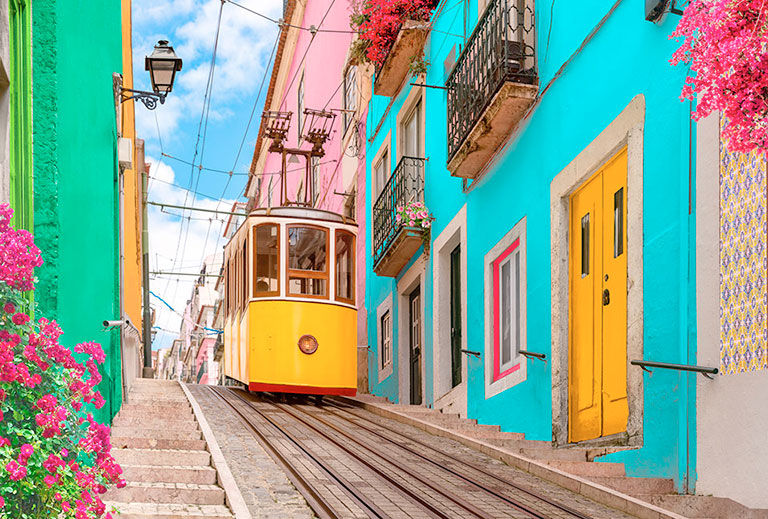 Yellow typical tram on a street with colorful houses and flowers on the balconies - Bica Elevator going down the hill of Chiado in Lisbon, Portugal.